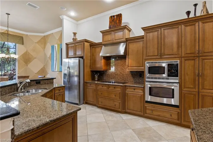 Kitchen with dark stone counters, stainless steel appliances, wall chimney range hood, sink, and backsplash