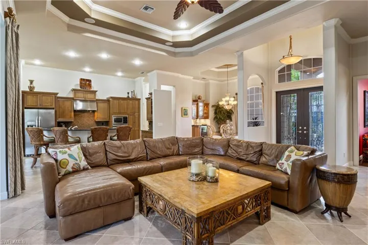 Tiled living room with french doors, crown molding, a raised ceiling, and ceiling fan