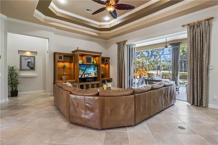 Tiled living room with ceiling fan, a raised ceiling, and ornamental molding