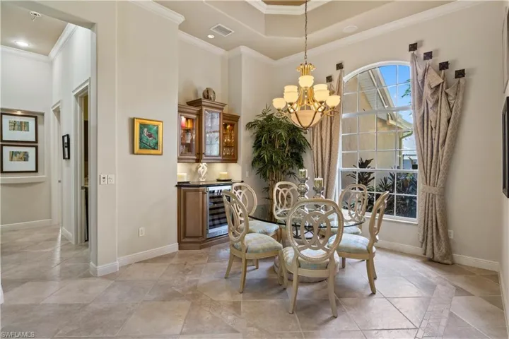 Tiled dining room featuring an inviting chandelier, crown molding, wine cooler, and a raised ceiling