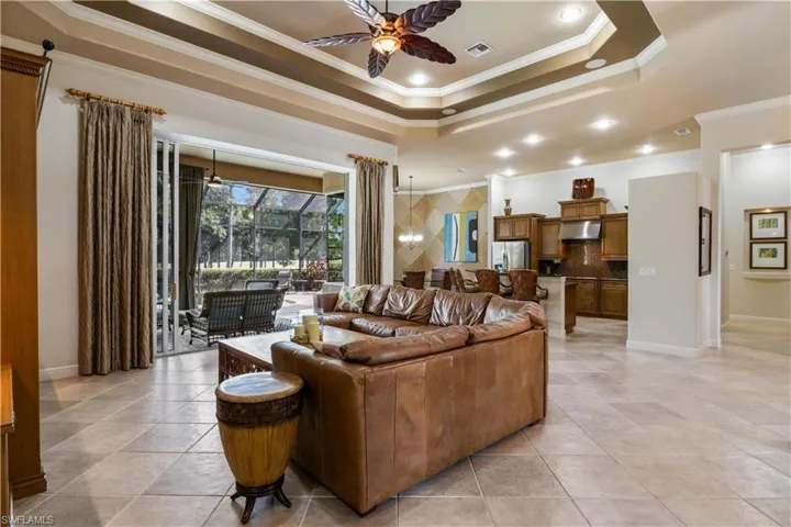 Living room featuring ceiling fan, a tray ceiling, ornamental molding, and light tile patterned floors