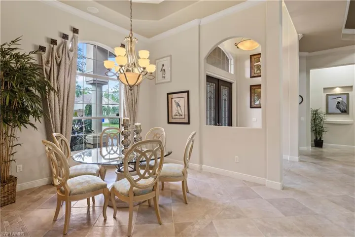 Tiled dining area featuring a towering ceiling, a notable chandelier, crown molding, and a tray ceiling