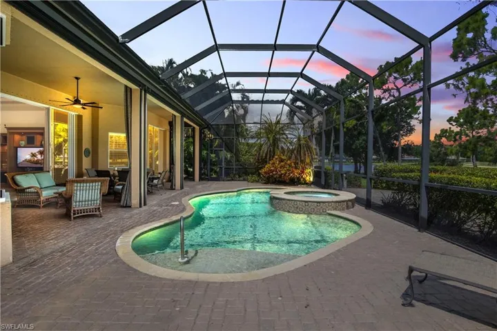 Pool at dusk with an in ground hot tub, a lanai, outdoor lounge area, a patio, and ceiling fan