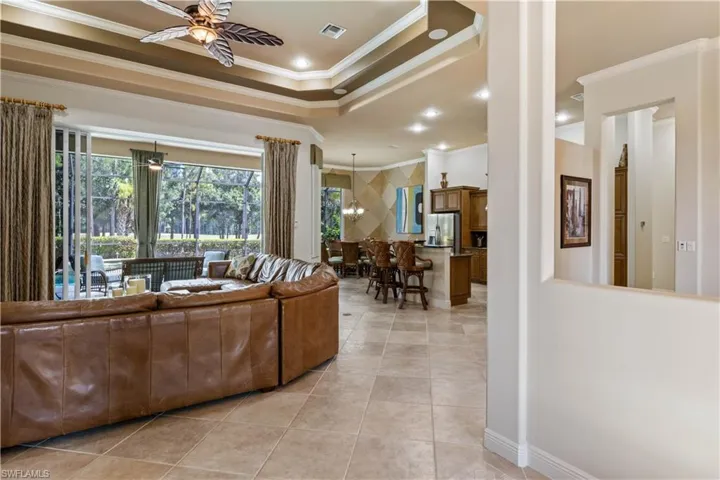 Living room featuring ceiling fan, crown molding, a tray ceiling, and light tile patterned floors