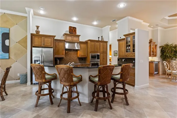 Kitchen with tasteful backsplash, crown molding, wall chimney exhaust hood, appliances with stainless steel finishes, and light tile patterned floors