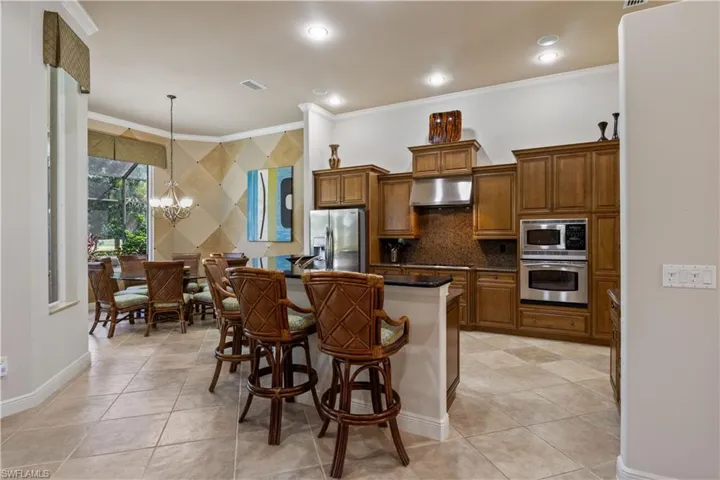 Kitchen with a chandelier, ornamental molding, stainless steel appliances, and wall chimney exhaust hood