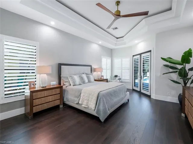 Bedroom featuring baseboards, visible vents, a raised ceiling, dark wood-type flooring, and access to outside