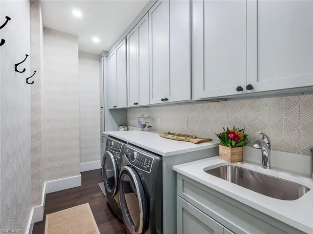 Laundry room featuring dark wood-style flooring, a sink, baseboards, independent washer and dryer, and cabinet space