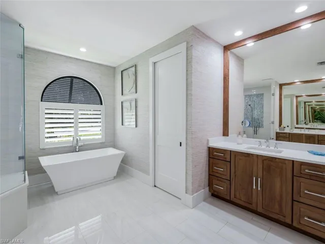 Bathroom with recessed lighting, visible vents, tile walls, vanity, and a soaking tub