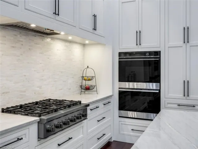 Kitchen featuring appliances with stainless steel finishes, white cabinets, backsplash, and light stone counters