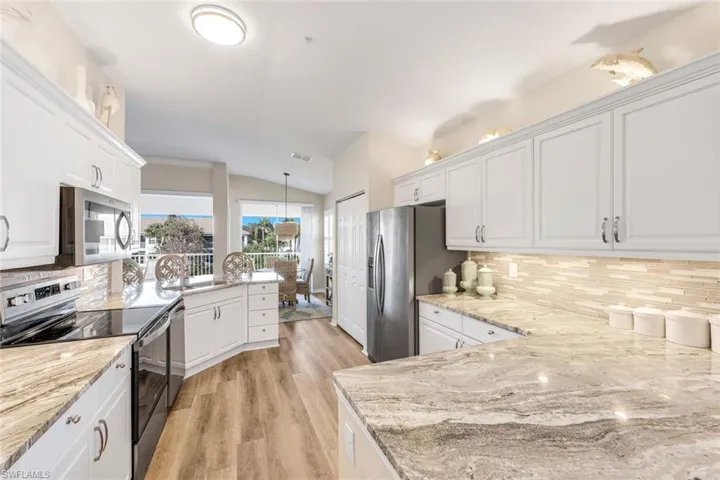 Kitchen with stainless steel appliances, white cabinetry, vaulted ceiling, a peninsula, and pendant lighting
