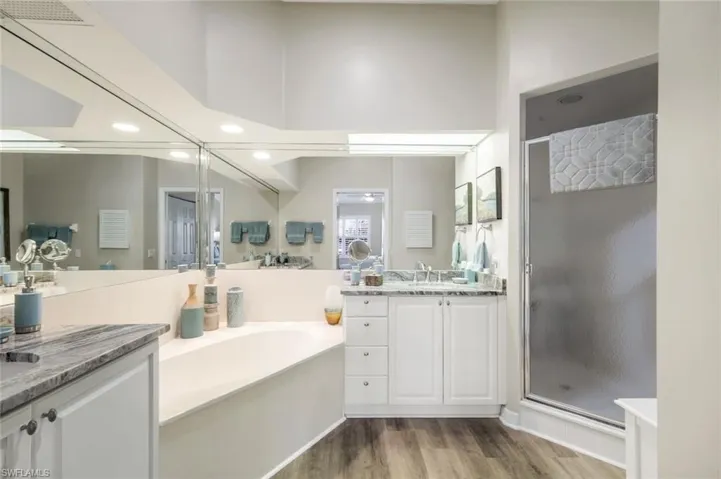 Bathroom featuring a stall shower, two vanities, light wood-type flooring, recessed lighting, and a bath