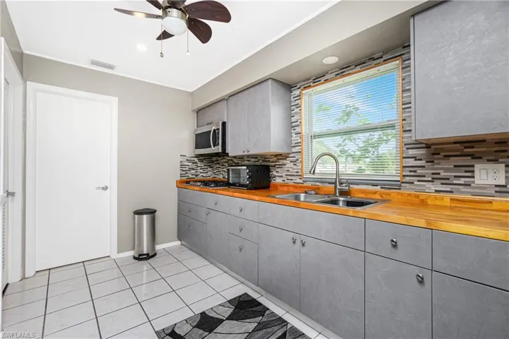 Kitchen featuring wood counters, sink, gray cabinets, light tile patterned floors, and stainless steel appliances