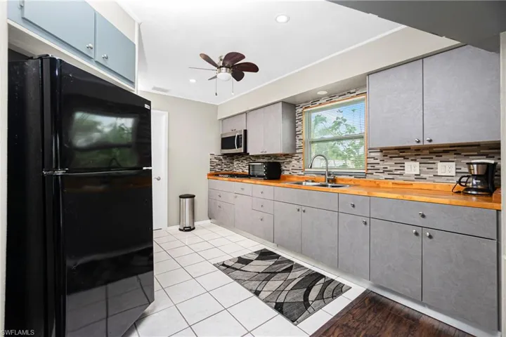 Kitchen featuring backsplash, black fridge, sink, ceiling fan, and butcher block countertops