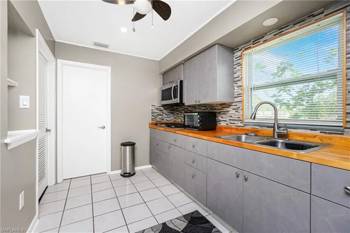 Kitchen with sink, appliances with stainless steel finishes, tasteful backsplash, butcher block countertops, and light tile patterned flooring