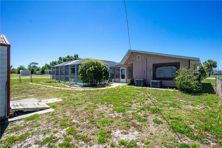 Rear view of house with a lanai, a lawn, central AC unit, and a pool