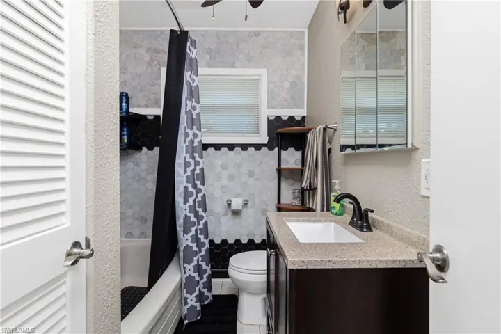 Full bathroom featuring vanity, shower / tub combo with curtain, ceiling fan, tile walls, and toilet