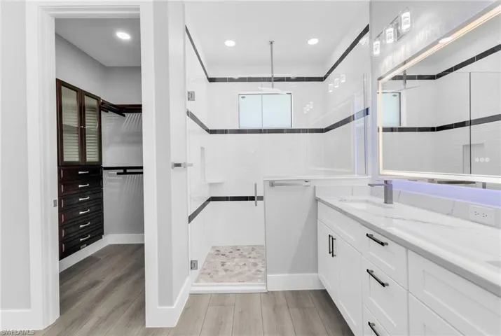 Full bathroom with a walk in closet, double vanity, a shower stall, light wood finished floors, and recessed lighting