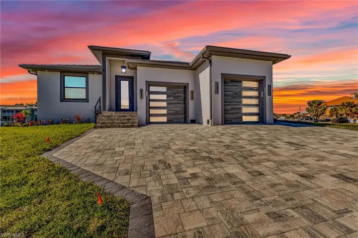 View of front facade with stucco siding, decorative driveway, an attached garage, and a lawn