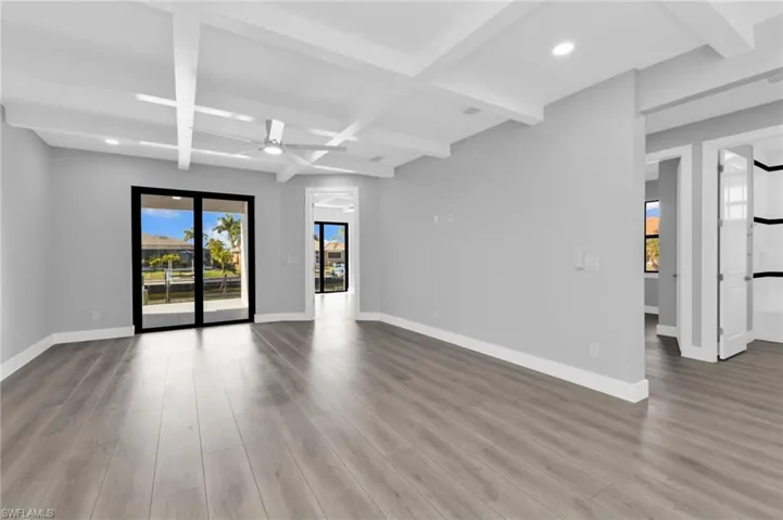 Spare room featuring beamed ceiling, healthy amount of natural light, ceiling fan, coffered ceiling, and light wood-type flooring