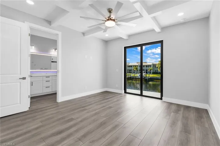 Empty room with a water view, coffered ceiling, beam ceiling, light wood finished floors, and recessed lighting