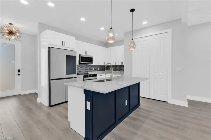 Kitchen with smart refrigerator, white cabinets, light stone counters, pendant lighting, and decorative backsplash