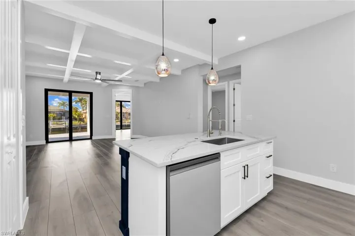 Kitchen featuring beamed ceiling, light stone countertops, stainless steel dishwasher, a center island with sink, and ceiling fan