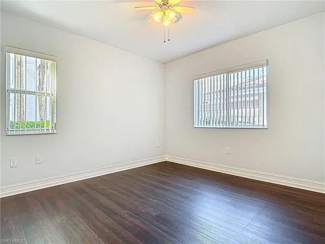Unfurnished room with baseboards, dark wood-style floors, and a ceiling fan