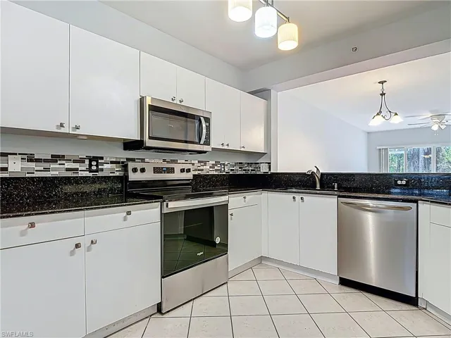 Kitchen with decorative backsplash, white cabinets, appliances with stainless steel finishes, and pendant lighting