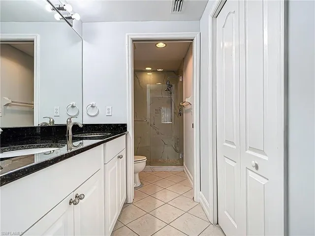 Full bath with a marble finish shower, visible vents, toilet, tile patterned floors, and vanity
