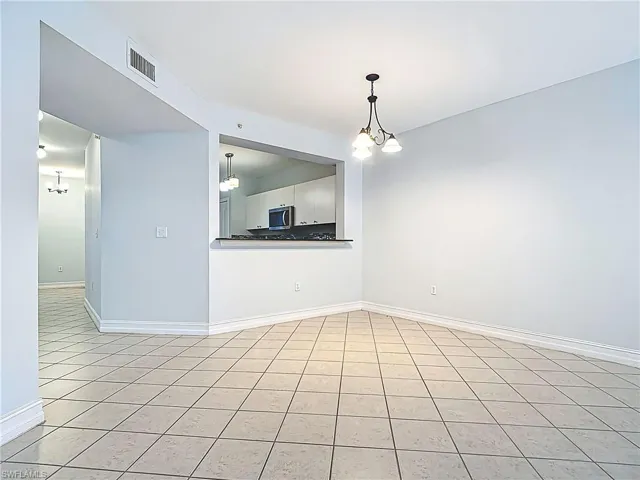 Unfurnished room featuring light tile patterned floors, visible vents, baseboards, and an inviting chandelier
