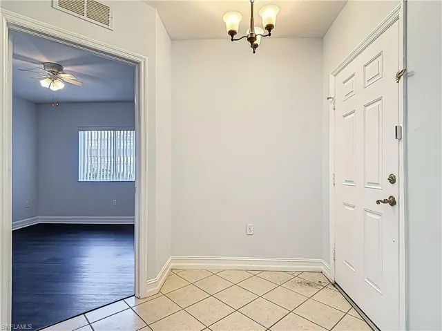 Entryway with light tile patterned floors, visible vents, baseboards, and ceiling fan with notable chandelier