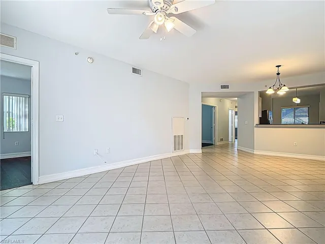 Unfurnished living room with light tile patterned floors, visible vents, ceiling fan with notable chandelier, and baseboards