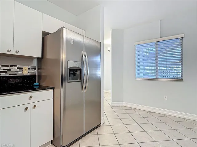 Kitchen featuring backsplash, white cabinetry, stainless steel fridge, light tile patterned flooring, and baseboards