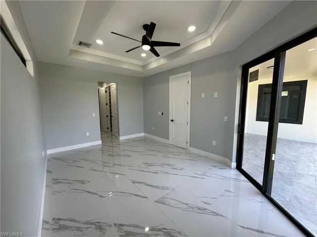 Tiled empty room featuring a healthy amount of sunlight, ceiling fan, and a raised ceiling