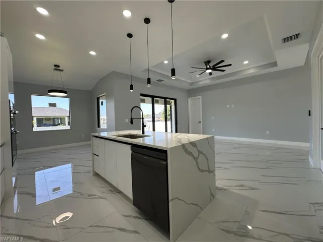 Kitchen featuring white cabinets, sink, black dishwasher, a raised ceiling, and a kitchen island with sink