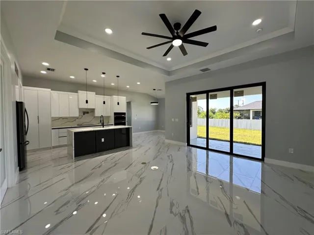 Kitchen featuring a center island with sink, fridge, light tile patterned floors, and a tray ceiling
