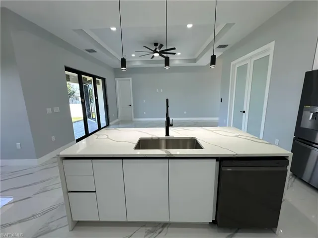 Kitchen with black dishwasher, white cabinetry, light stone countertops, and a tray ceiling