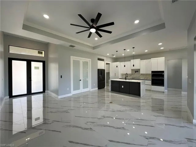 Kitchen with french doors, a raised ceiling, a center island with sink, and white cabinets