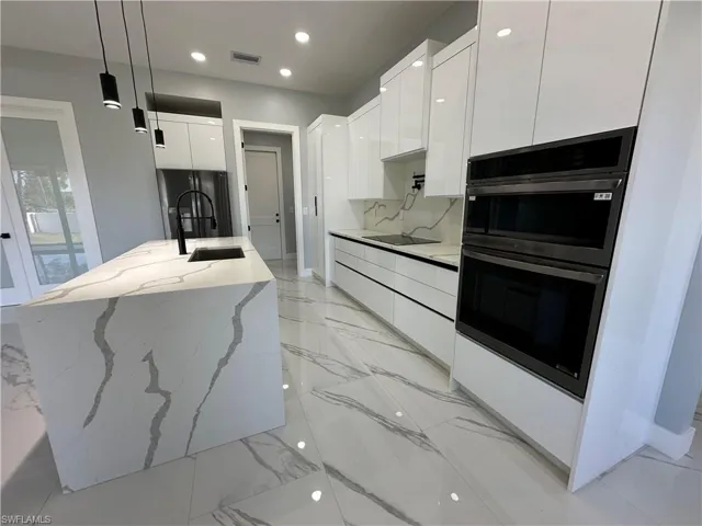 Kitchen with decorative light fixtures, black appliances, tasteful backsplash, sink, and light stone counters