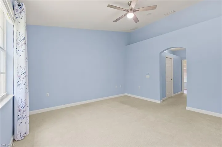 Unfurnished room featuring arched walkways, light colored carpet, a ceiling fan, and baseboards