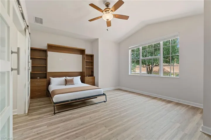 Bedroom featuring light wood-type flooring, lofted ceiling, baseboards, and a ceiling fan