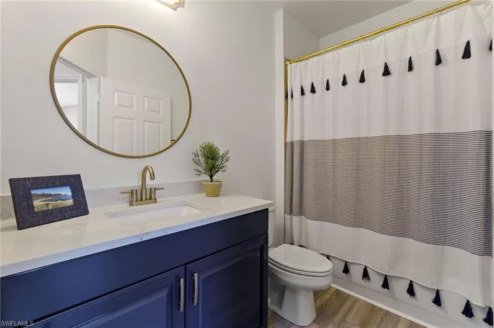 Bathroom with wood finished floors, toilet, vanity, and shower / bath combination with curtain