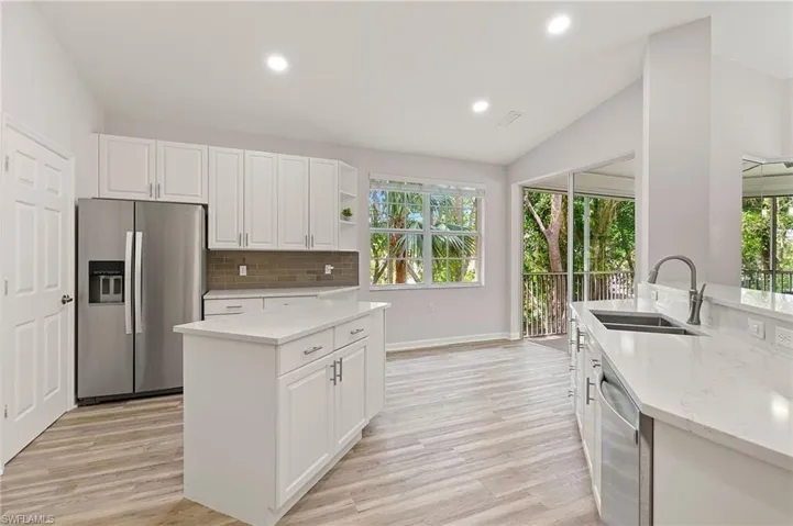 Kitchen featuring appliances with stainless steel finishes, a sink, vaulted ceiling, light stone counters, and tasteful backsplash