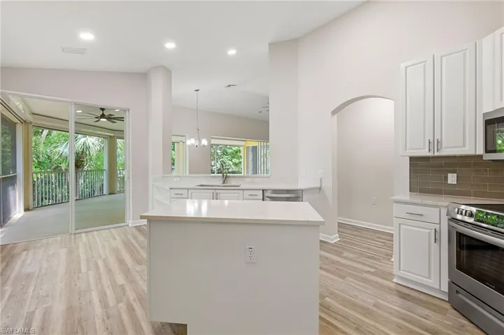 Kitchen featuring appliances with stainless steel finishes, a sink, backsplash, light wood finished floors, and lofted ceiling
