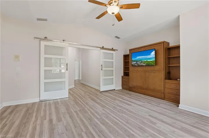 Unfurnished living room with a barn door, ceiling fan, lofted ceiling, light wood-style flooring, and baseboards