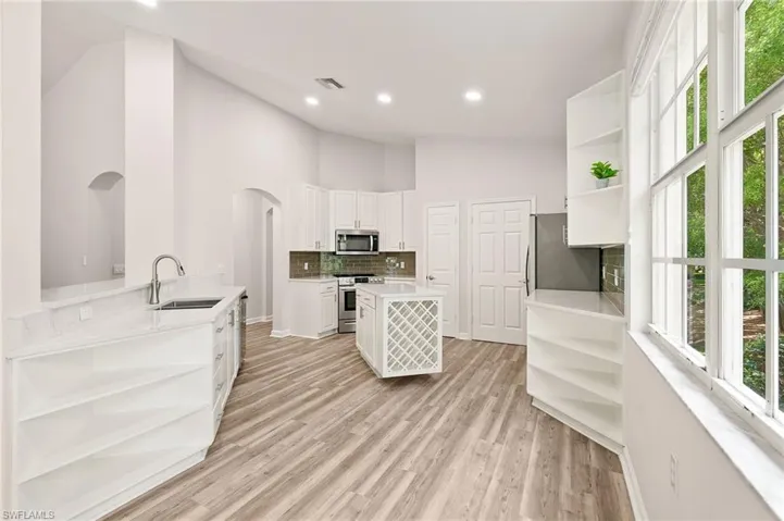 Kitchen with open shelves, stainless steel appliances, a sink, decorative backsplash, and healthy amount of natural light