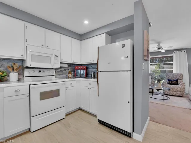 Kitchen with light hardwood / wood-style floors, backsplash, white cabinetry, white appliances, and ceiling fan