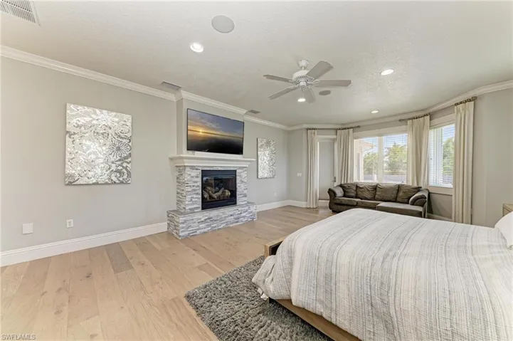 Bedroom with wood finished floors, a glass covered fireplace, baseboards, and visible vents