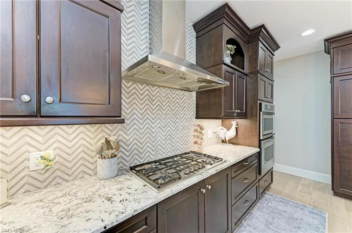 Kitchen featuring baseboards, wall chimney range hood, stainless steel appliances, and dark brown cabinets